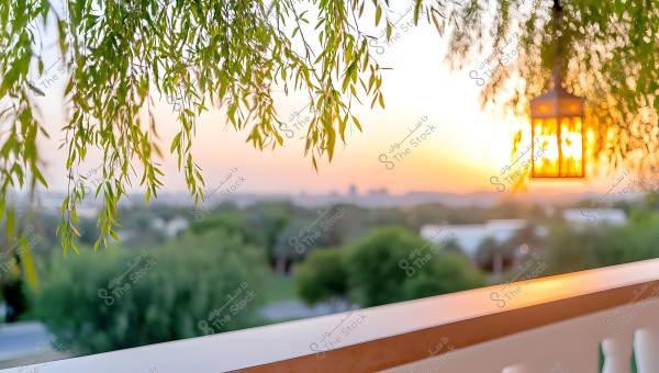 An image depicting a natural scene at sunset, with green tree leaves hanging down from the top on the left side. The background extends to the horizon with warm colors in the sky. A glowing lantern is hanging on the right side of the image. In the foreground, there is a wooden railing.
