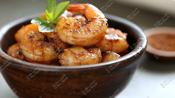 An image shows a wooden bowl containing well-seasoned cooked shrimp. The shrimp is garnished with small green leaves, adding a touch of color and harmony to the dish.