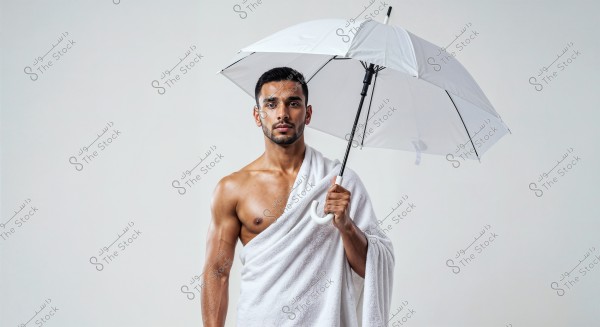 A portrait of a man standing, holding a white umbrella and wearing a white fabric draped over his upper body. The image features a simple white background, and the man is posed facing the camera directly.
