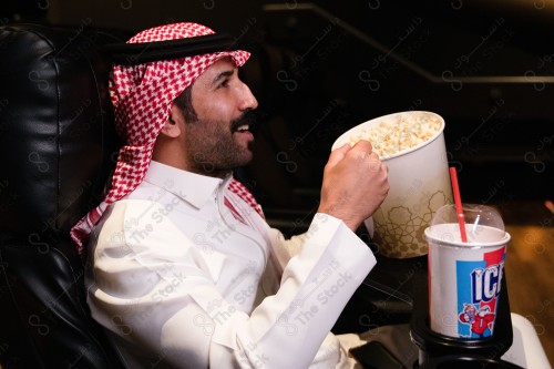 شاب سعودي يرتدي الزي السعودي التقليدي  ويشاهد أحد الأفلام المعروضة بينما يتناول من الفشار