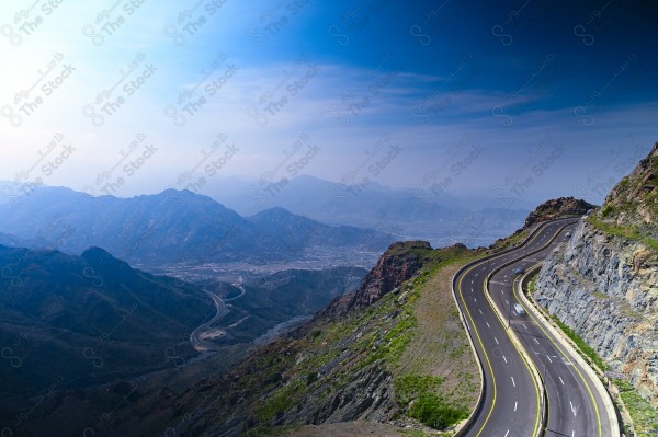 A snapshot of a series of towering rocky mountains and paved roads extending in the Al Hada Mountains in Taif, showing a cloudy sky during the day, mountain heights, Taif Mountains, mountain range