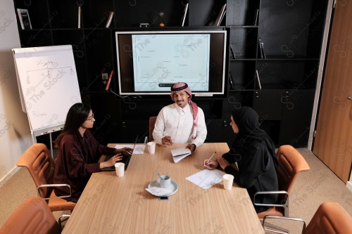 A Saudi man in traditional Saudi dress holds a meeting with Saudi female employees wearing abaya in the meeting room