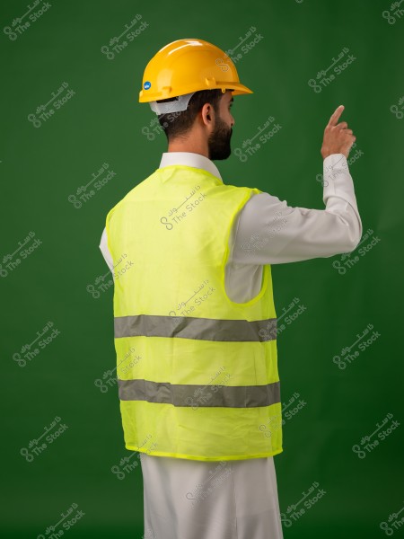 رجل يرتدي سترة أمان صفراء وخوذة بناء صفراء, يشير بيده على خلفية خضراء.