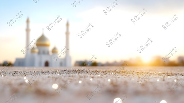 A scene of a desert in the foreground with a focus on shimmering grains of sand. In the blurred background, there is a mosque with golden domes and tall minarets, set against a blue sky with a soft sunlight glow on the horizon.