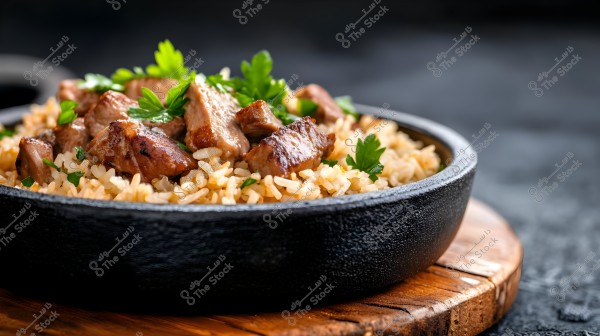A dish of rice with pieces of meat served in a black bowl on a wooden base. The rice is accompanied by grilled meat pieces and green parsley leaves.