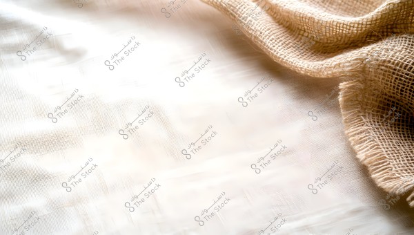 An image of light brown burlap fabric on a smooth, light-colored surface. The fabric is shown in detail, illustrating a woven, net-like pattern. Natural lighting highlights the intertwined fibers of the fabric.