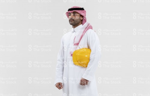 بورتريه مهندس سعودي يحمل خوذة المهندسين على يديه ويرتدي الزي السعودي الرسمي على خلفية بيضاء