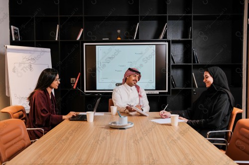 A Saudi man in traditional Saudi dress holds a meeting with Saudi female employees wearing abaya in the meeting room