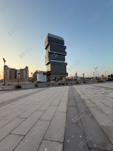 صورة لناطحة سحاب بتصميم معماري عصري متدرج, محاطة ببعض المباني الأخرى. يظهر في الصورة أيضًا جزء من طريق ألواح حجرية في المقدمة, وتبدو السماء صافية مع إضاءة نهارية طبيعية.\r\n\r\n-