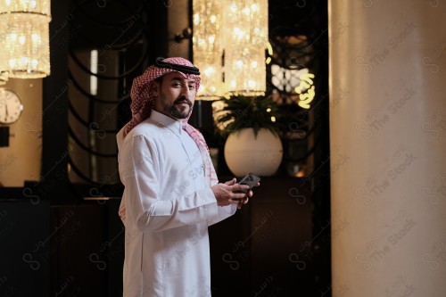 شاب سعودي في استقبال الفندق ، ويقوم بتعابير مختلفة باستخدام الجوال  ، ويقوم بدفع عبر جهاز الدفع الالكتروني ،