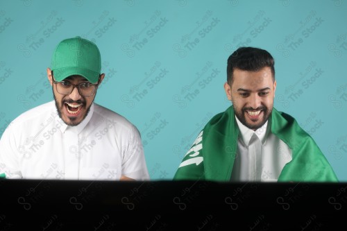 شابان سعوديان يشاهدان مباراة ويشجعان المنتخب السعودي على خلفية تركوازيه بكل فرح و حماس، كأس العالم.