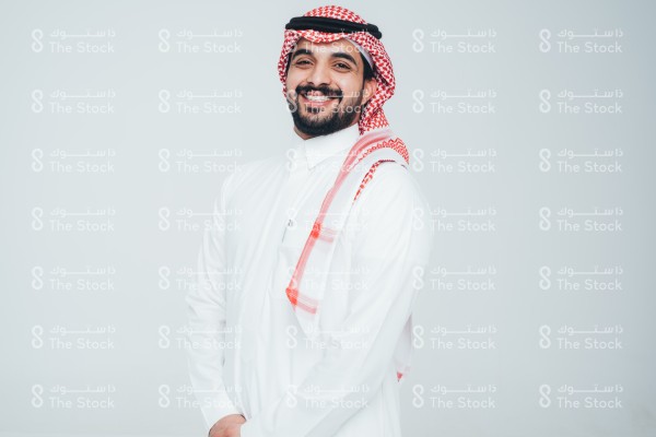 بورتريه رجل سعودي يرتدي الثوب ويقف أمام خلفية بيضاء، يتفاعل بحركات تعبيرية بيديه