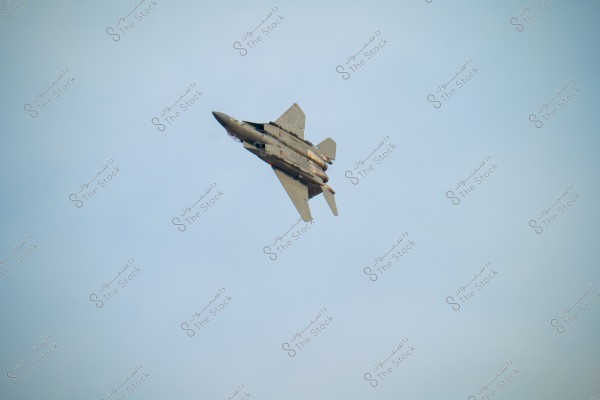 An image of an F-15 fighter jet flying in the blue sky. The aircraft is in a tilted position, highlighting its aerodynamic design against the cloudless background.