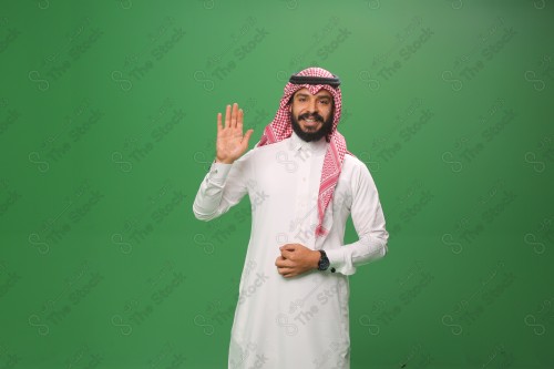 رجل سعودي يقف على خلفية خضراء يرتدي الثوب و الشماغ، يقوم بعمل حركات بيديه يلقي التحية بيده اليمنى وهو مبتسم، احتفالات العيد