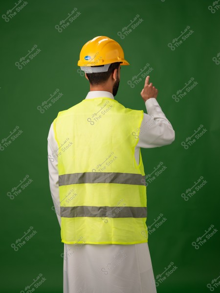 شخص يرتدي خوذة صفراء وسترة أمان عاكسة يقف ويشير بيده.