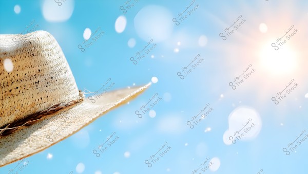 A straw hat with a wide brim is shown on the left side of the image, with a clear blue sky and bright sun in the top right corner. Light passes through the hat, creating a luminous glow and sparkling flecks scattered in the air.