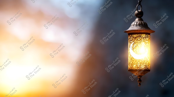 A traditional hanging lantern, decorated with Arabic patterns and a crescent, glowing with warm colors. The background is blurred with a mix of blue and orange hues, creating a calm and soothing atmosphere.