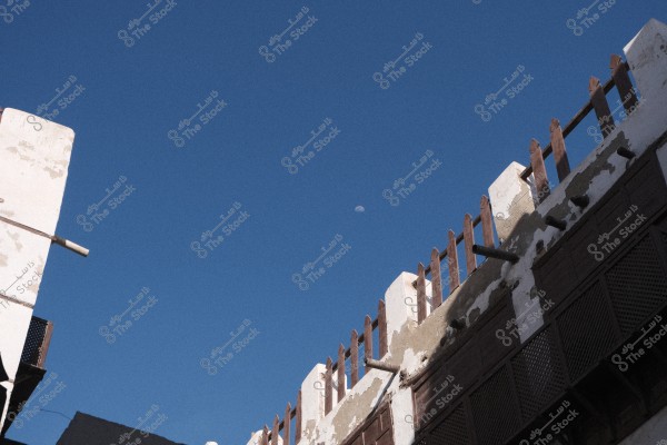 A blue sky with the moon in the background and part of an old building with a weathered wooden facade.