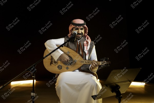 رجل يعزف على العود ويرتدي الثوب السعودي التقليدي, يجلس أمام ميكروفون.