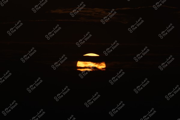 A sunset scene where the sun partially emerges from behind thick layers of dark clouds. The bright orange sun is partially obscured by the clouds in a dark sky, creating a dramatic contrast of colors.