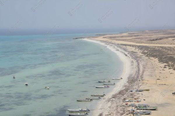 An image of a Red Sea shoreline featuring white sandy beaches and clear turquoise waters. Several small boats are docked near the shore, with some resting on the sand. In the background, the expansive coastline is visible with desert terrain and sparse vegetation.