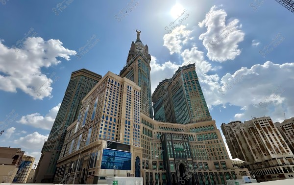 صورة لمجمع أبراج  البيت تضم ساعة كبيرة في مكة, السعودية, مع سماء زرقاء وبعض السحب في الخلفية.