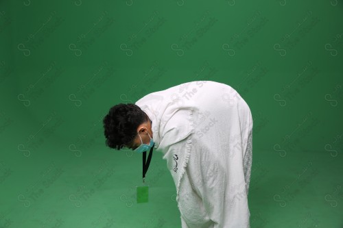 Portrait of a pilgrim with white skin on a green background, wearing Ihram to perform Hajj, performing the duty of prayer