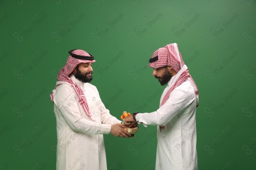 رجل سعودي يرتدي الزي السعودي التقليدي يقدم سلة الحلوى لضيفه في أحد المناسبات