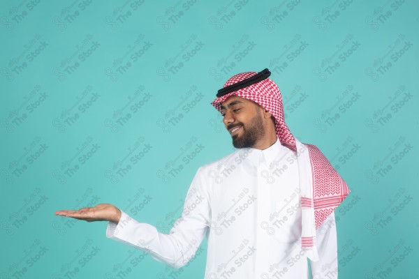 بورتريه رجل يرتدي الثوب ويقف أمام خلفية تركوازي ، مبتسم ، يتفاعل بإشارات تعبيرية بيديه