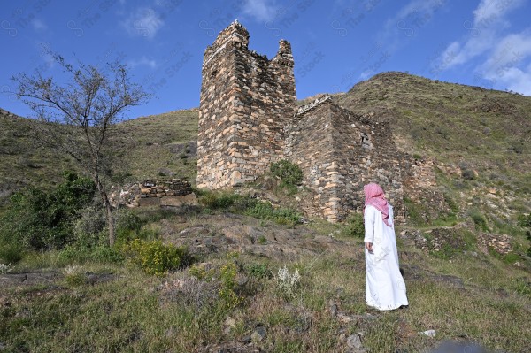 A shot of a Saudi man wearing the Saudi dress, meditating and standing on one of the green mountains.