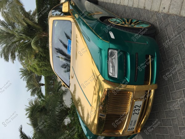 An image of a luxury car with a shiny design, combining green and gold colors, parked on a paved brick road. The car has a license plate from Dubai. In the background, there are lush green palm trees, indicating a warm climate and a setting of opulence.