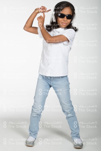 Portrait of a Saudi girl standing on a white background, wearing a headset and wearing sunglasses, listens to music and dances with enthusiasm.  happy girl