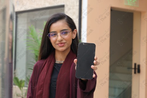 A Saudi woman wearing an abaya holds a mobile phone and displays its screen