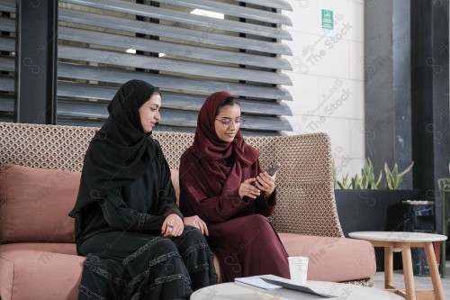 A Saudi woman wearing an abaya holds a mobile phone and displays its screen