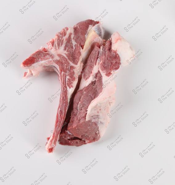 Pieces of raw meat placed on a white surface. The meat has some fat, and the bone is visible in the pieces.