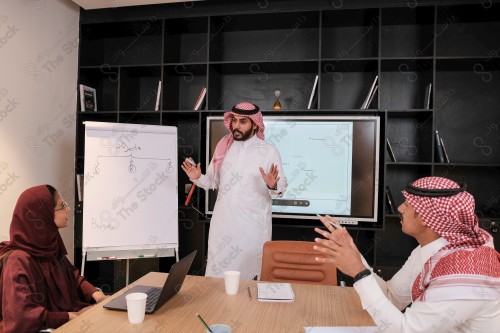 A Saudi man in traditional Saudi dress conducts a business meeting in the boardroom during the day