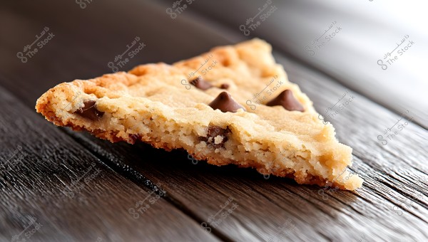A triangular piece of chocolate chip cookie rests on a dark wood surface.  Perfect for baking blogs, recipe websites, or food packaging