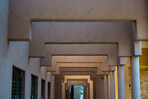 A heritage corridor built of mud, a group of columns appears on the right of the corridor, while there are a group of windows on the left during the day