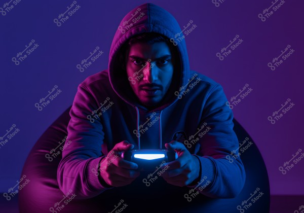 ** An image of a man wearing a hoodie sitting on a bean bag chair, tightly holding a video game controller, under blue and purple neon lights casting over his face. His serious expression indicates intense focus on the game.\r\n\r\n- **