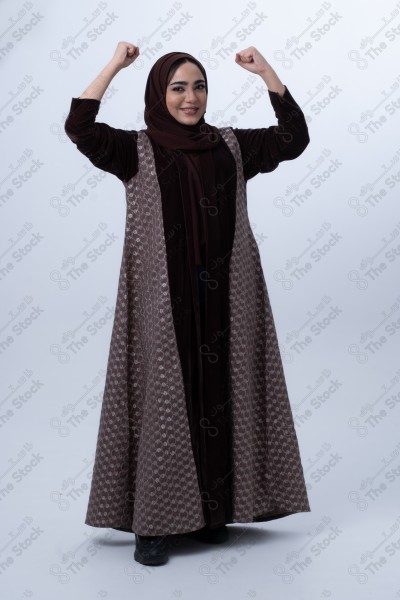 Portrait of a young Saudi woman wearing an abaya and hijab, with a smiling facial expression, standing against a white background