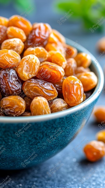 An image of a blue ceramic bowl filled with glistening golden and brown dates. The dates are arranged attractively, with soft shadows of green leaves in the background, adding a sense of freshness and warmth.