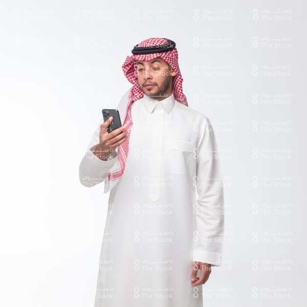 رجل سعودي يرتدي الزي السعودي يستخدم جواله على خلفية بيضاء