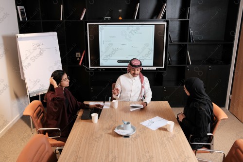 A Saudi man in traditional Saudi dress holds a meeting with Saudi female employees wearing abaya in the meeting room