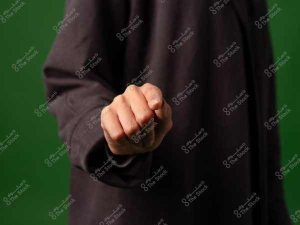 يد شخص مقبوضة في إشارة إلى القوة أو التهديد, الخلفية خضراء.