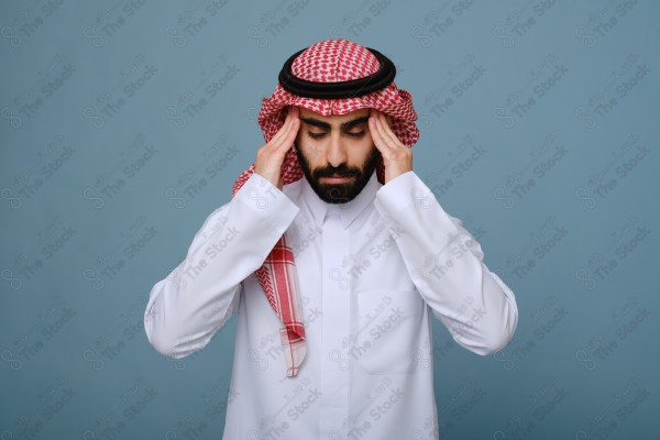 بورتريه شاب سعودي يرتدي الزي السعودي على خلفية سماوية، يمسك رأسه ، يشعر بالصداع ،آلام الصداع والمرض.