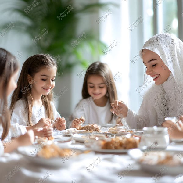 An image of a mother wearing a white hijab smiling at her children as they sit around a naturally lit dining table. The children, dressed in white, are happily enjoying the meal together. In the background, there are green plants and daylight coming through a nearby window.
