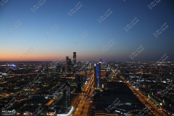 A nighttime photograph of a large city featuring towering skyscrapers and illuminated streets. The skyline showcases distinctive architectural lines, with city lights sparkling beneath the dark sky. The horizon displays a slight hint of sunset glow.\r\n\r\n###