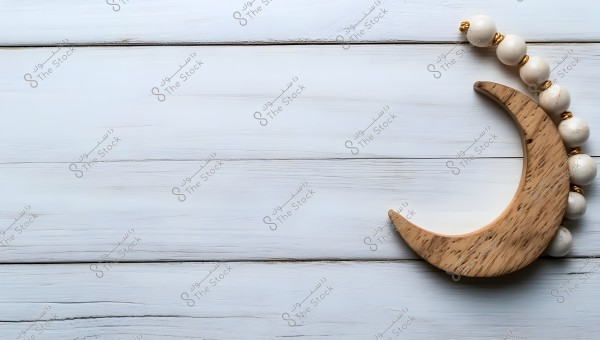 Image of a carved wooden crescent shape placed on a light wooden surface. The crescent is adorned with large white beads interspersed with small golden rings.