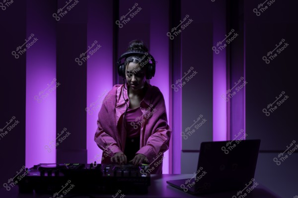 ديدجي ترتدي سماعات رأس وتعمل على معدات صوتية تحت إضاءة خلفية بنفسجية.