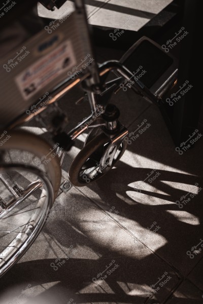 Close-up image of a metallic wheelchair on a sunlit floor, with prominent shadows of the wheels.